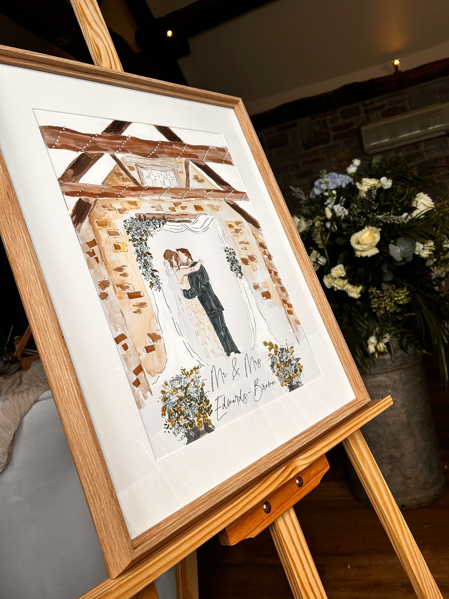 Framed hand-painted venue illustration displayed on an easel at a wedding reception